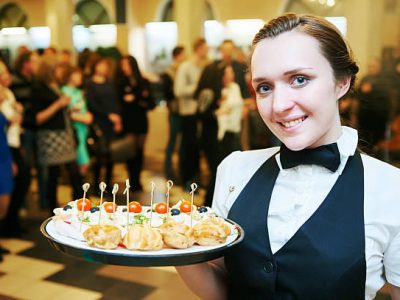 Catering service. Restaurant waitress girl with food tray at event. Natural authentic shot in challenging light condition.